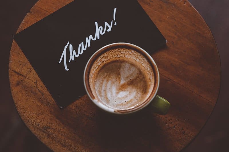 A coffee cup on a table with a card that says thanks. Showing proper appreciation will help you get more engagement with customers.