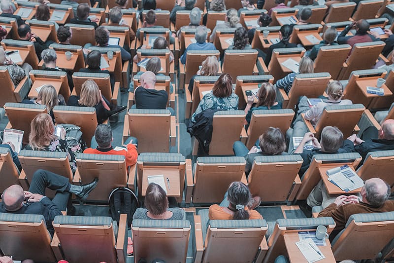People sitting in chairs in a large lecture hall room.