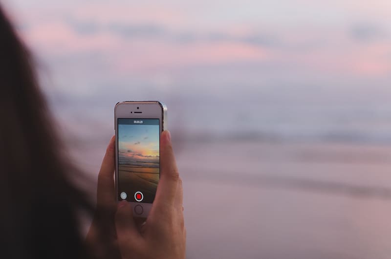Person recording a beach sunset on their phone.