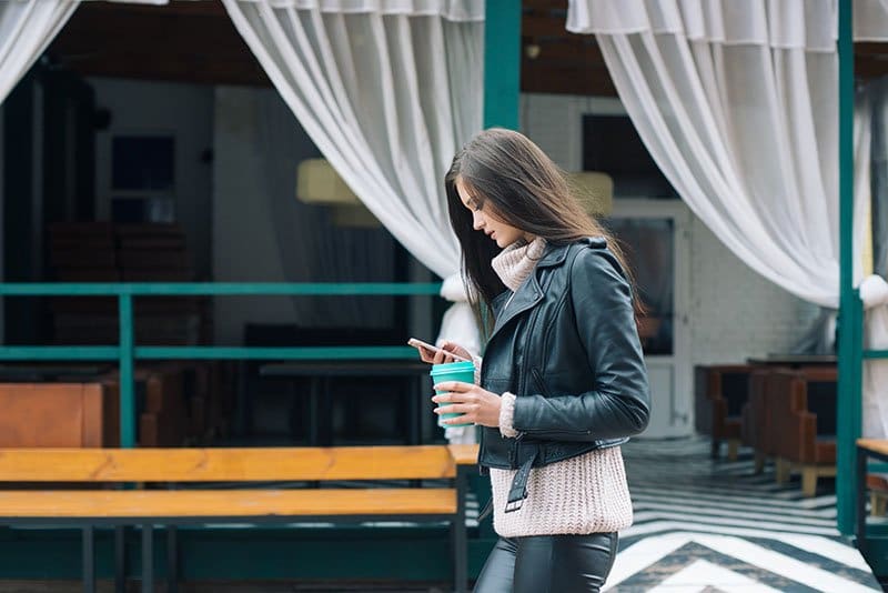 A woman walking while looking at her phone and holding a coffee cup. To get more engagement with customers, you need to have real conversations.